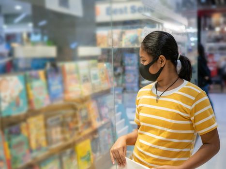 Long haired girl Wear a protective mask Looking at the showcase In a bookstore. Concept of life And protect yourself from the coronavirus outbreak.