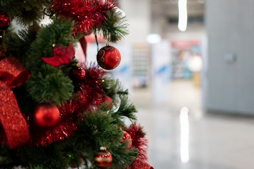 Close Christmas tree in a shopping center against the background of blurry shop windows. Free space for text