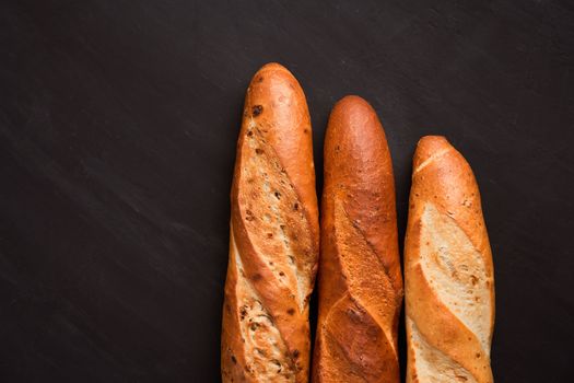 Three crispy french baguettes lie dark black table background sesame seeds Classic french national pastries Copy space Concept for menu or advertising