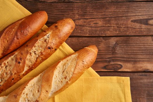 Three crispy french baguettes lie yellow cloth napkin wooden table background baguettes in assortment with sesame seeds Classic french national pastries Copy space Concept for menu or advertising