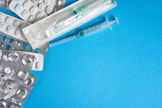 Empty used blisters from tablets silver and white color and pills lie on blue medical background. Pharmaceutical Concept Health care and medicine. free Copy space Medical plastic disposable syringe.