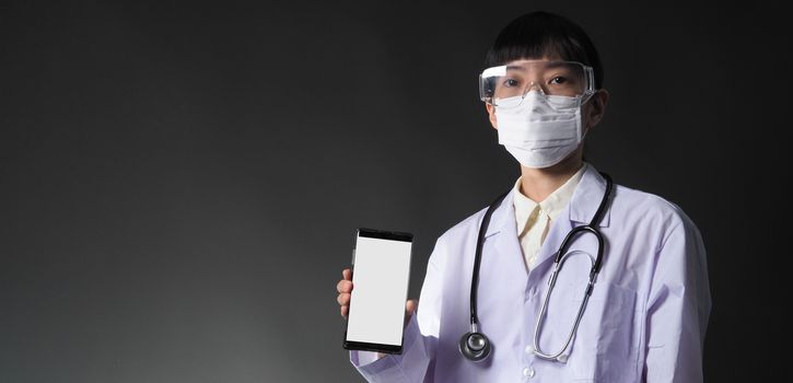 Middle aged of asian woman doctor showing mobile phone screen to communicate something. And she wearing white lab suit, mask and goggle to prevent coronavirus or covid-19