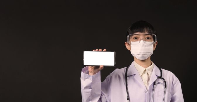 Middle aged of asian woman doctor showing mobile phone screen to communicate something. And she wearing white lab suit, mask and goggle to prevent coronavirus or covid-19