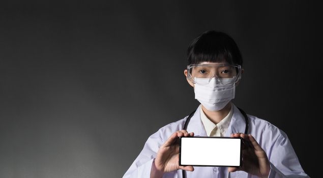 Middle aged of asian woman doctor showing mobile phone screen to communicate something. And she wearing white lab suit, mask and goggle to prevent coronavirus or covid-19