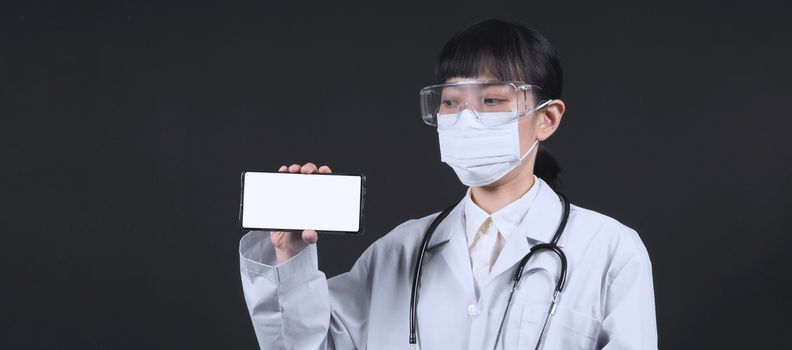 Middle aged of asian woman doctor showing mobile phone screen to communicate something. And she wearing white lab suit, mask and goggle to prevent coronavirus or covid-19