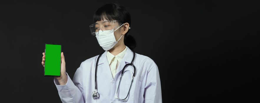 Middle aged of asian woman doctor showing mobile phone screen to communicate something. And she wearing white lab suit, mask and goggle to prevent coronavirus or covid-19