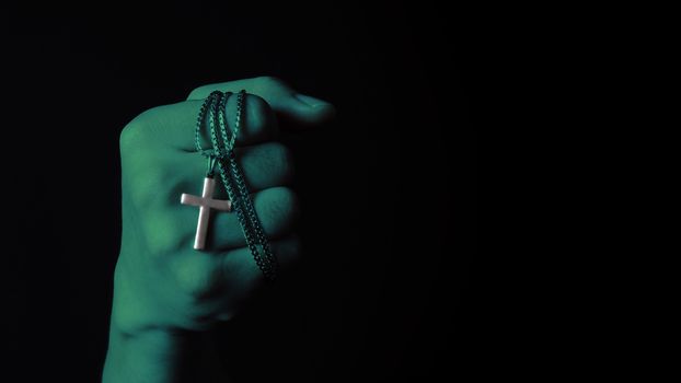 Crucifix pendant or cross sign made from silver and hold in man hand. represent praying for someone that pass away from World pandemic coronavirus and close-up shot black background 