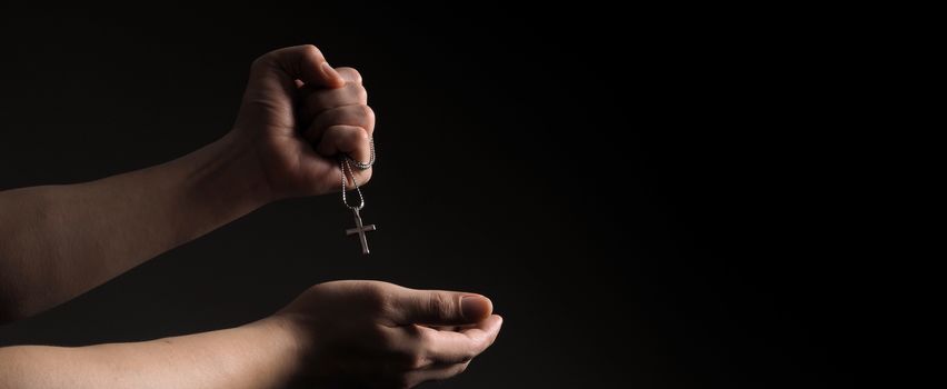 Crucifix pendant or cross sign made from silver and hold in man hand. represent praying for someone that pass away from World pandemic coronavirus and close-up shot black background 