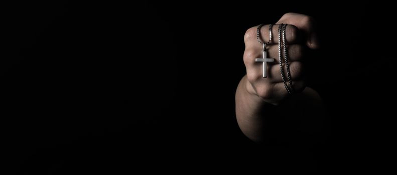 Crucifix pendant or cross sign made from silver and hold in man hand. represent praying for someone that pass away from World pandemic coronavirus and close-up shot black background 