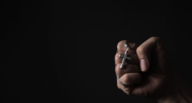 Crucifix pendant or cross sign made from silver and hold in man hand. represent praying for someone that pass away from World pandemic coronavirus and close-up shot black background 