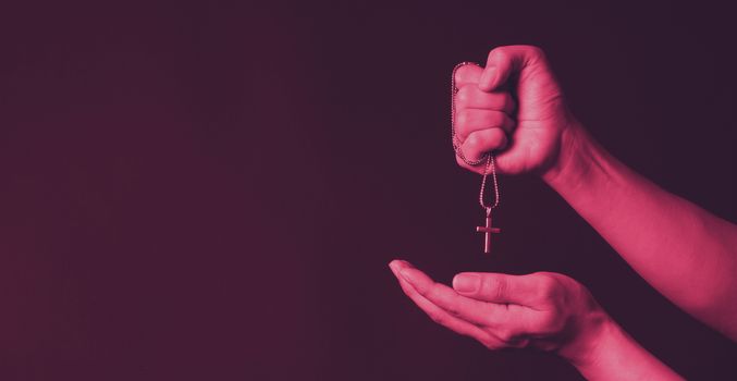 Crucifix pendant or cross sign made from silver and hold in man hand. represent praying for someone that pass away from World pandemic coronavirus and close-up shot black background 