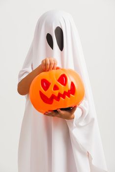 Funny Halloween Kid Concept, little cute child with white dressed costume halloween ghost scary he holding orange pumpkin ghost on hand, studio shot isolated on white background