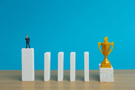 Miniature business concept - businessman thinking in front of obstacle wall to reach golden trophy