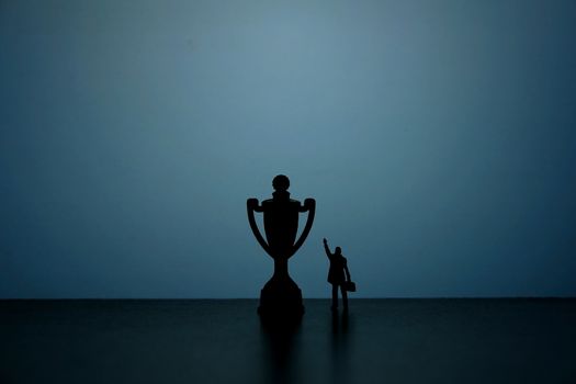 Business strategy conceptual photo - Silhouette of miniature businessman pointing on winning trophy