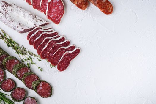 Variety of dry cured fuet and chorizosalami sausages, whole and sliced on white textured background, topview with space for text.