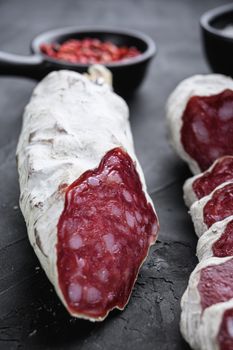 Dry cured salchichon sausage slices with herbs on balck background.