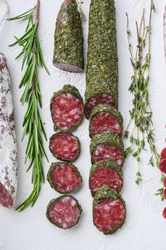 Variety of dry cured fuet and chorizosalami sausages, whole and sliced on white textured background, topview.