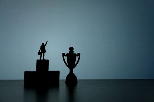 Business strategy conceptual photo - Silhouette of miniature businessman standing on podium pointing on trophy