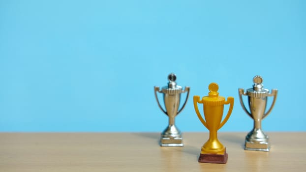 Golden trophy with two silver trophy at back above wooden table