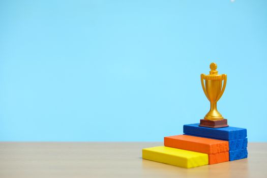 Golden trophy standing at colorful podium on wooden table