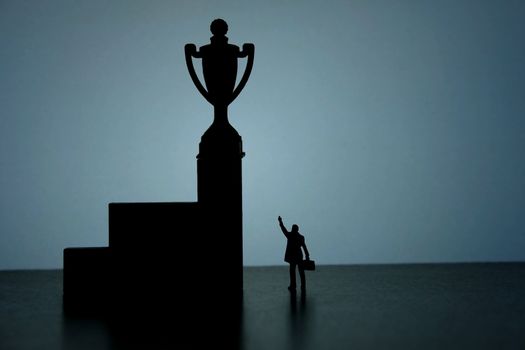 Business strategy conceptual photo - Silhouette of miniature businessman pointing on winning trophy in the podium