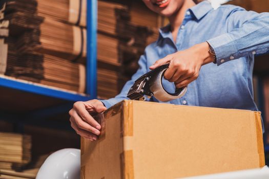 Closeup of Warehouse worker woman packing cardboard box with sticky tape with Indian worker man in local warehouse or factory, industry and export business concept, partner and colleague work together