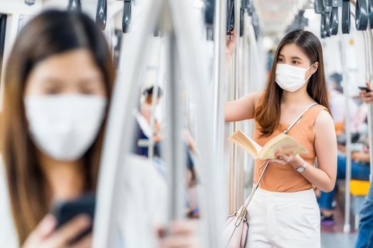 Young Asian woman passenger wearing surgical mask and reading the book in subway train when traveling in big city at Covid19 outbreak, Infection and Pandemic concept