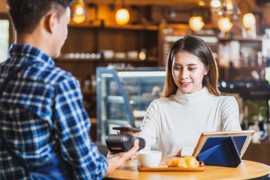 Asian customer man paying with credit card via contactless nfs technology to Asian Barista of Small business owner at the table in coffee shop, Small business owner and startup in coffee shop concept