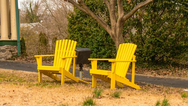 Two Yellow Wooden Lawn Chairs With a Small Tree In between Them