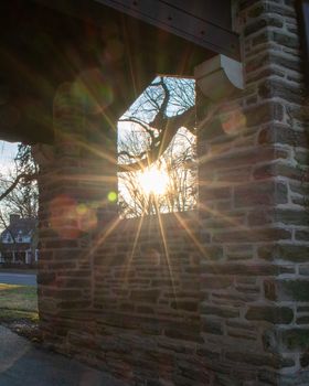 The Sun Shining Through a Window in a Cobblestone Wall in a Suburban Neighborhood