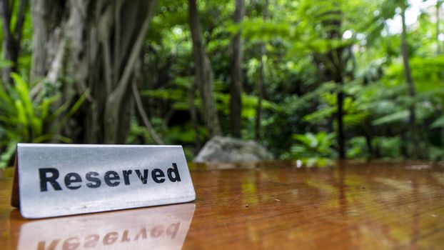 Reserved sign made out stainless steel plate on a laminated wooden table of a restaurant with trees and forest in the background.