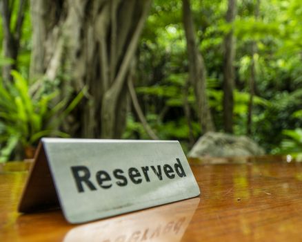 Reserved sign made out stainless steel plate on a laminated wooden table of a restaurant with trees and forest in the background.