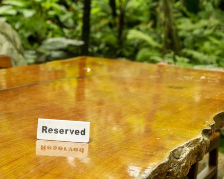 Reserved sign made out stainless steel plate on a laminated wooden table of a restaurant with trees and forest in the background.