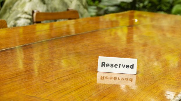 Reserved sign made out stainless steel plate on a laminated wooden table of a restaurant with trees and forest in the background.