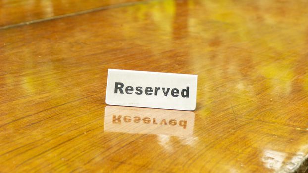 Reserved sign made out stainless steel plate on a laminated wooden table of a restaurant with trees and forest in the background.