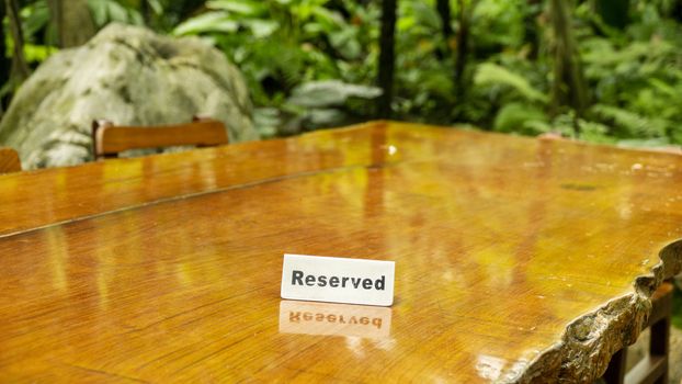 Reserved sign made out stainless steel plate on a laminated wooden table of a restaurant with trees and forest in the background.