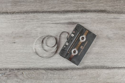 Liptovsky Hradok, Slovakia - March 10, 2018: Table top view on old compact cassette on gray wooden desk, with some tape pulled out.