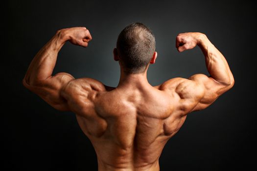 Young bodybuilder man flexing back double bicpes pose, showing his huge trapezius, rhomboid, levator and latissimus dorsi muscles. Studio shot on black background.