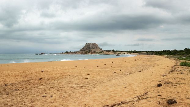 Beach with single hill (Patanangala rock) in distance on overcast day, storm coming in background. Yala National Park, Sri Lanka