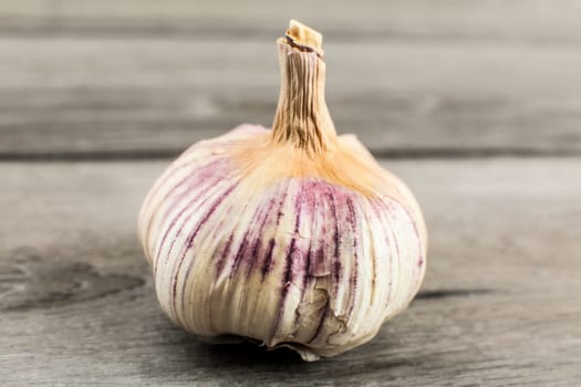 Single garlic bulb, cloves covered in purple skin with crack, on a gray wooden table.