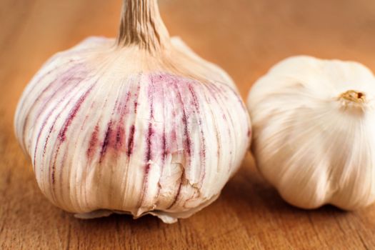 Single garlic bulb, cloves covered in purple skin with crack, on a dark wooden table.