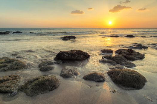 Wet sand on empty beach in golden sunset light during low tide showing rocks covered with sea algae. Kantiang Bay, Ko Lanta, Thailand.