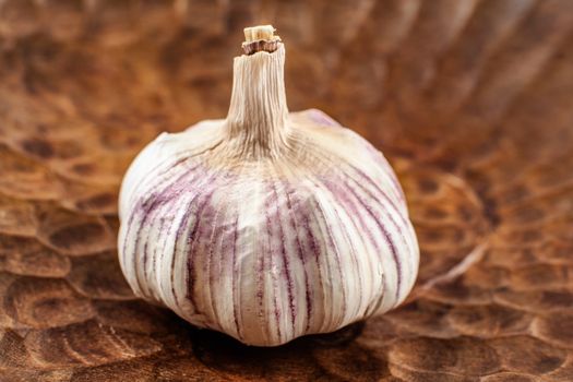 Detail on garlic bulb, cloves under purple skin, in an old wood bowl.