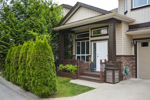 Main entrance of luxury residential house with doorsteps and small front yard behind green hedge