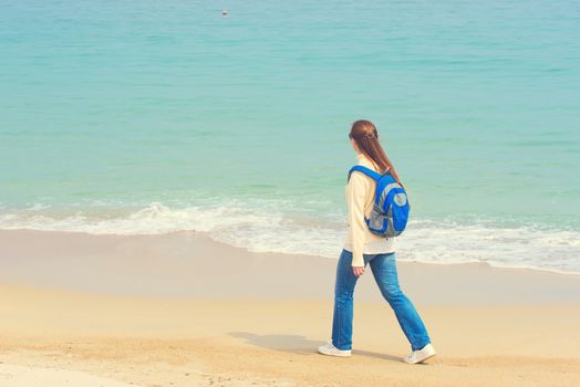 Girl with backpack walking along the beach. Young woman traveler