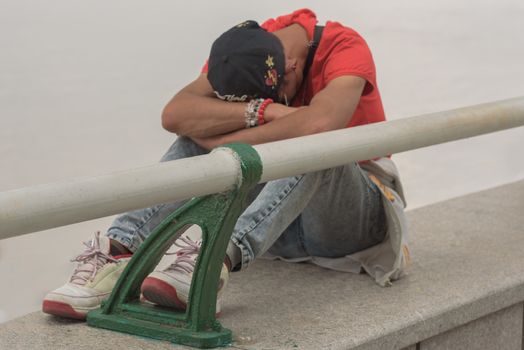 Harbin, Heilongjiang, China - September 2018: Young boy sitting alone with sad feeling. Guy sitting on the bridge