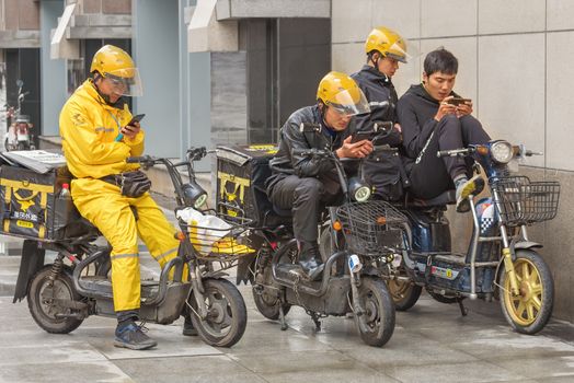Harbin, Heilongjiang, China - September 2018: Delivery man on motor scooter. Guys look at smartphones