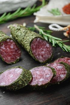 Variety of dry cured chorizo, fuet and other sausages cut in slices with herbs on dark wooden background.