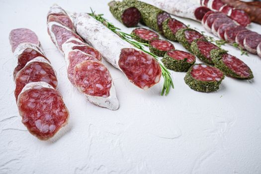 Variety of dry cured fuet and chorizosalami sausages, whole and sliced on white surface.