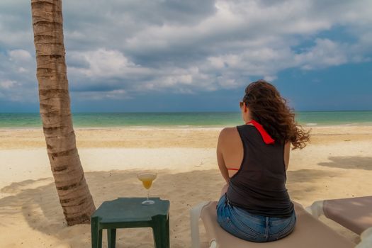 Woman sitting on a cot while contemplating the horizon of the blue sea. Holidays